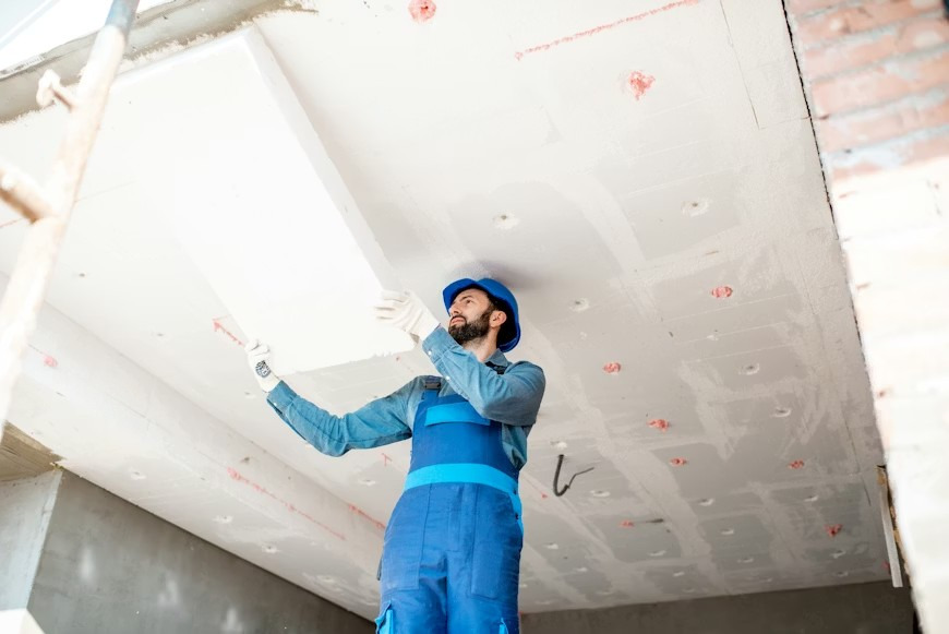 A builder is insulating a building's ceiling by mounting polystyrene sheets.