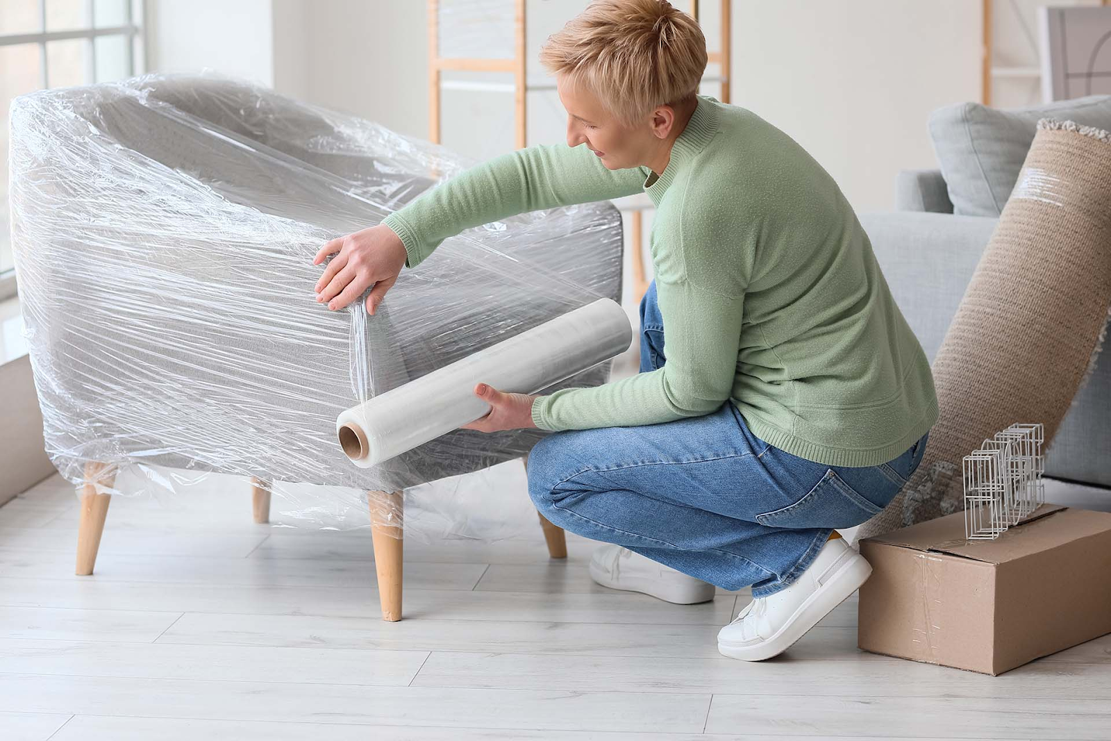 A person wraps an armchair in a large bubble wrap while preparing for a move.