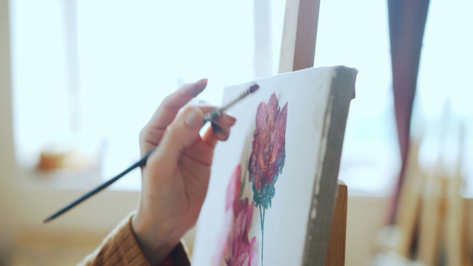 Closeup of a person painting roses on a canvas