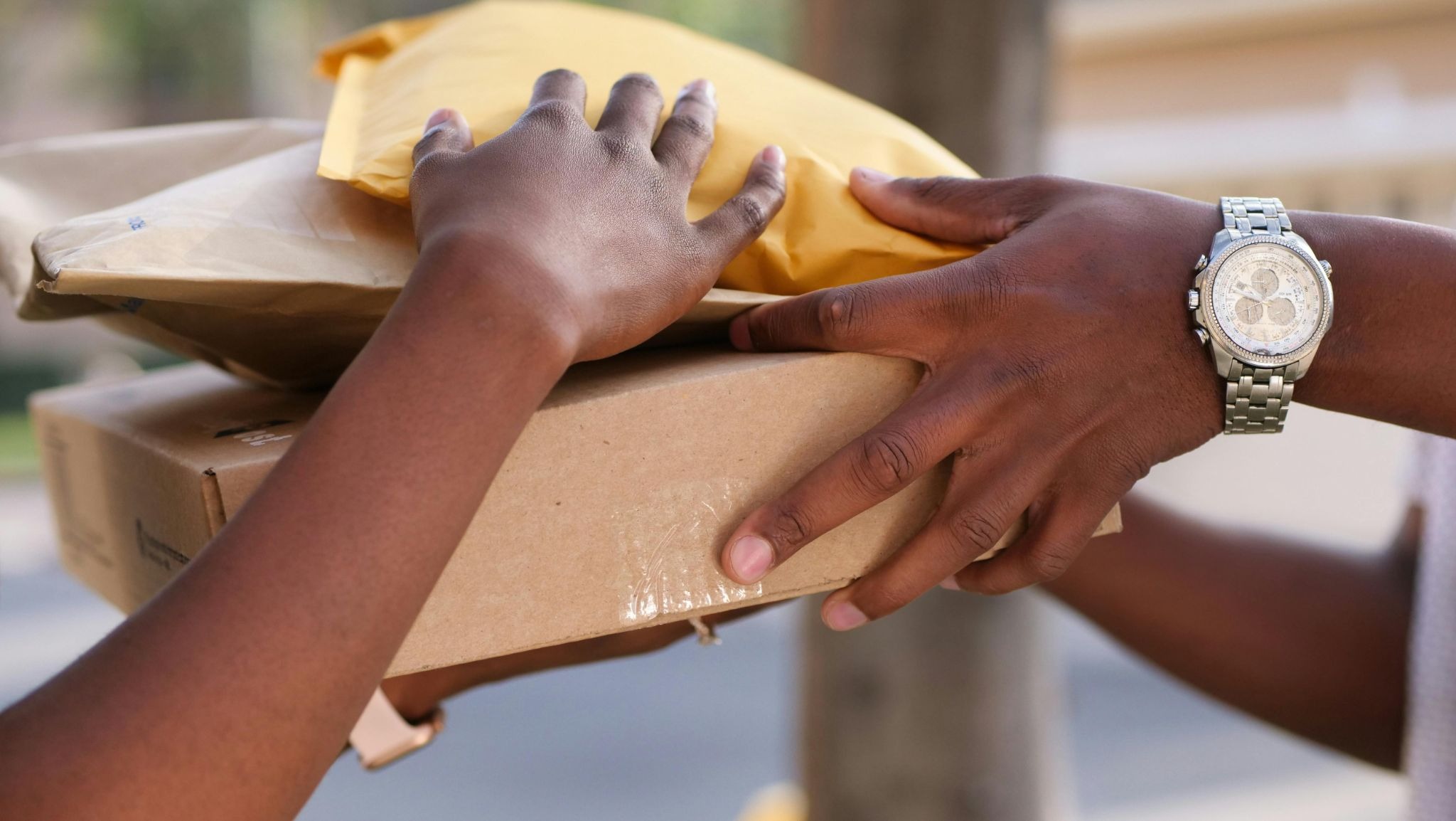 Two people holding 2 padded envelopes and 1 box of items