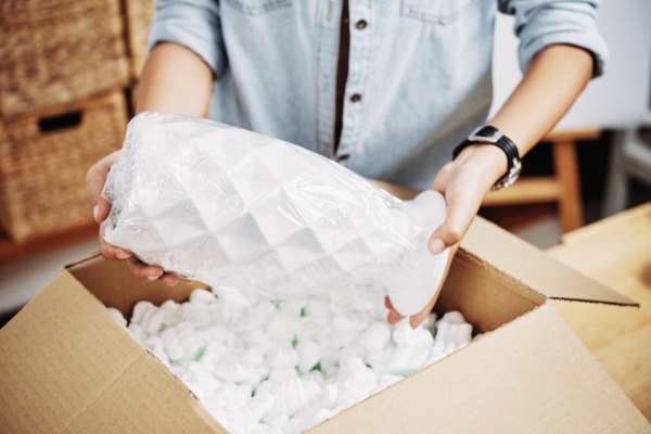 Woman packing vase in box with packaging peanuts