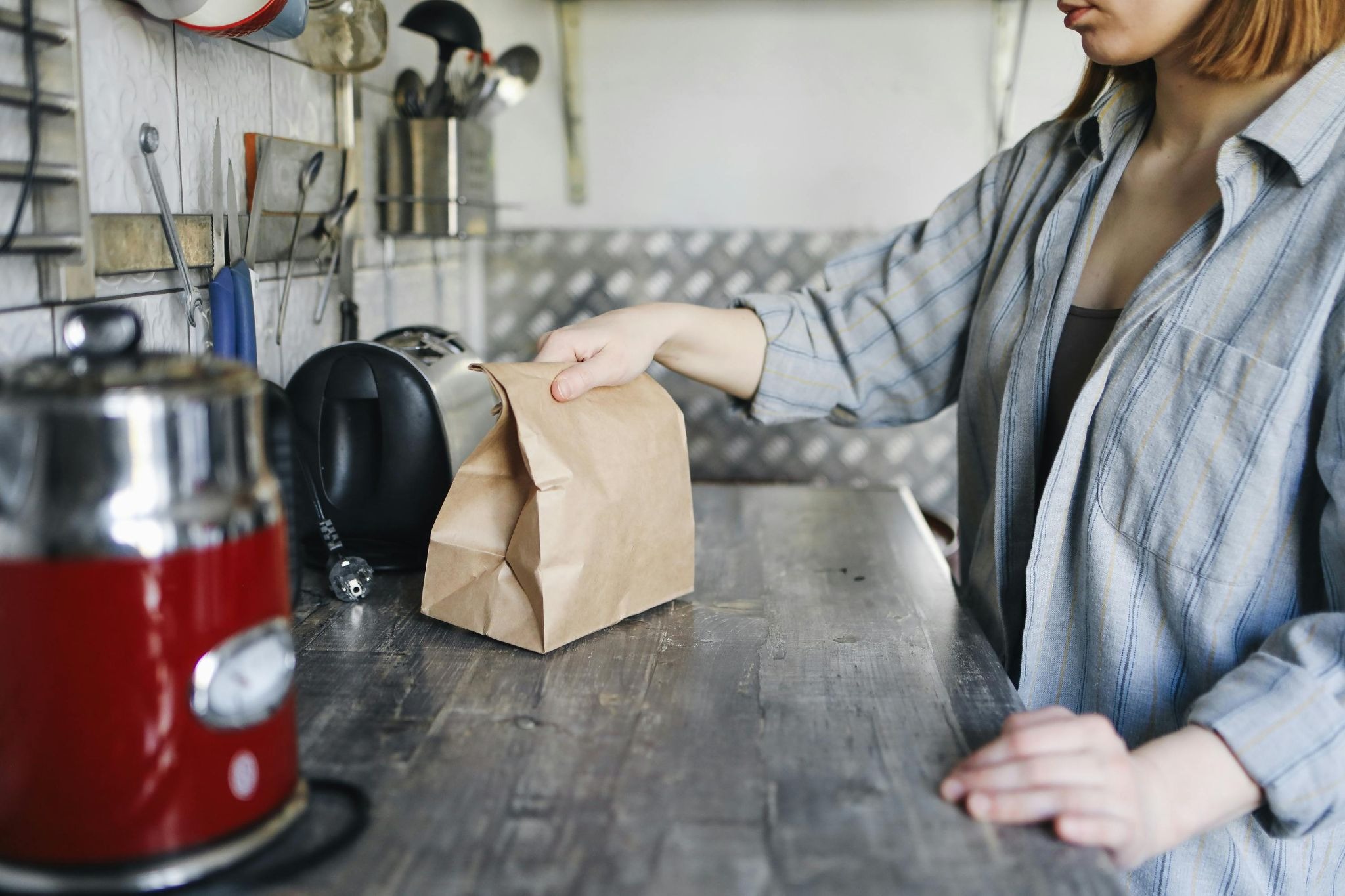 Woman holding a flat kraft stringed bag packed with food and placed on a kitchen counter