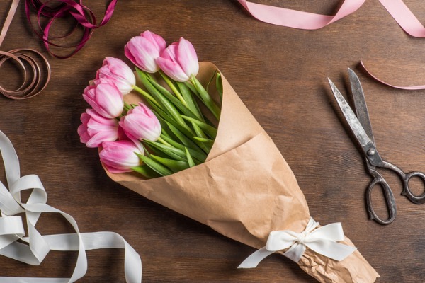 Tulips wrapped in brown kraft paper at a work station with ribbons and scissors