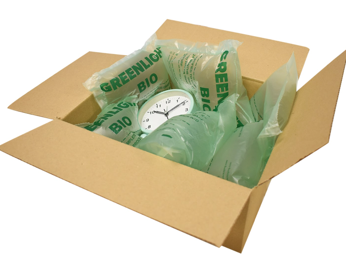 Open cardboard box filled with green biodegradable air pillows cushioning a small clock inside.