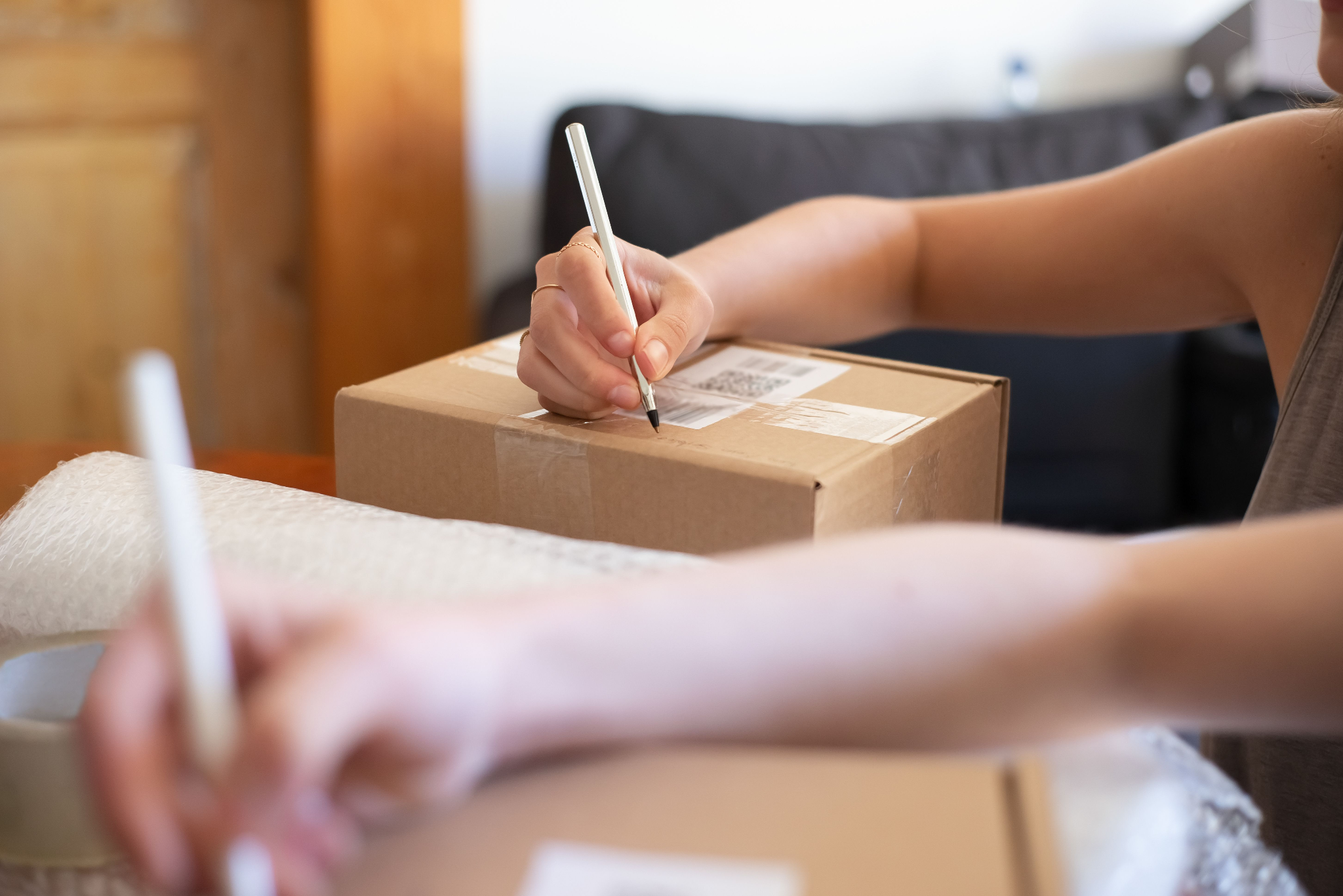 Two people are labelling cardboard boxes with bubble wrap nearby.