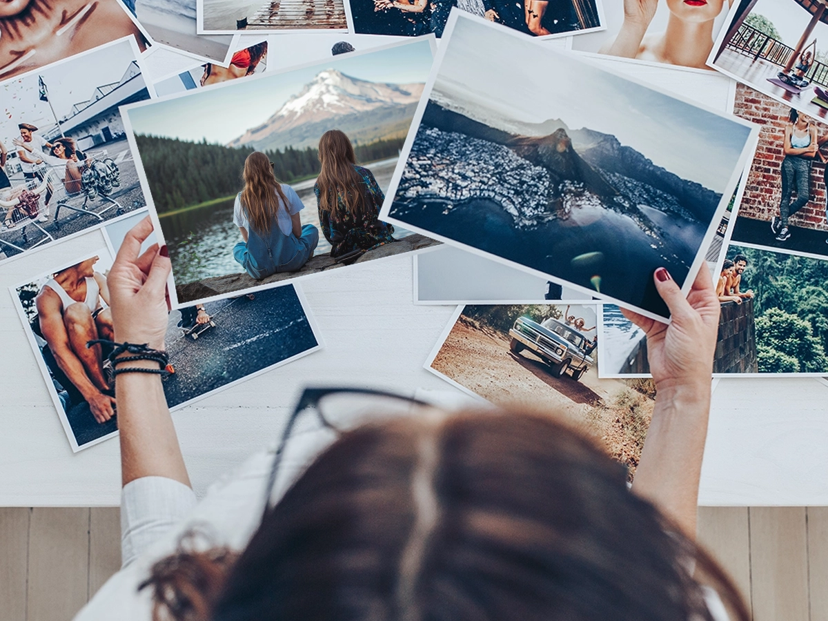 Person reviewing a spread of printed travel photos on a white table before packing them for mailing.