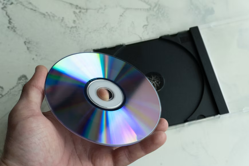Hand holding a CD/DVD disc with its case on a marble surface.