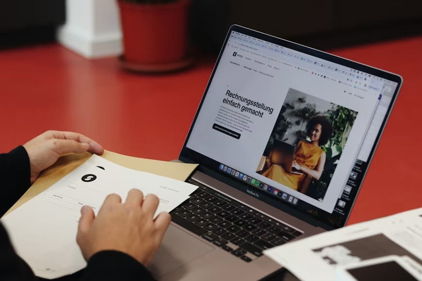 A person preparing to seal a document inside an envelope with a laptop opened in front of them. 