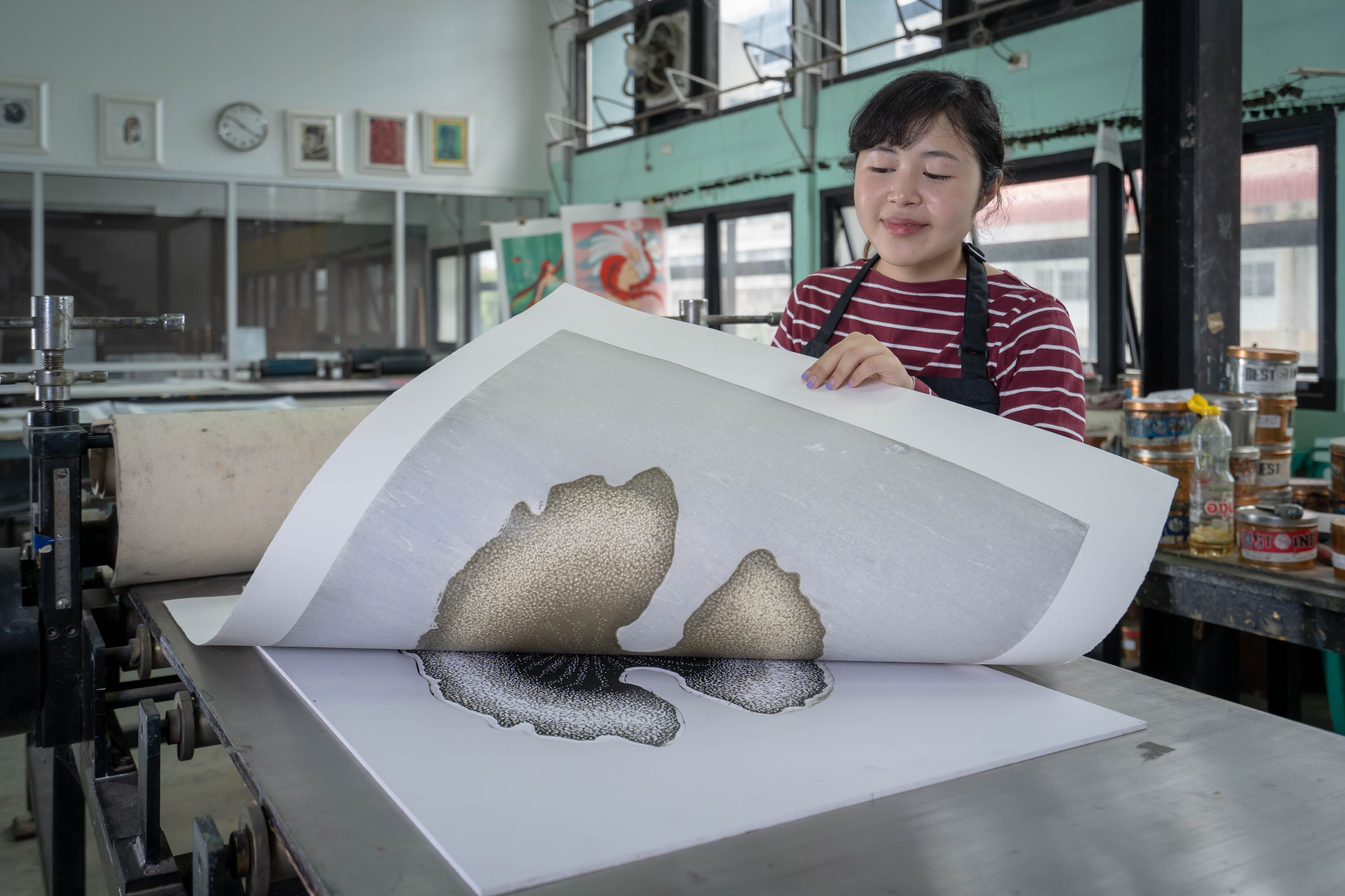 Printmaker lifting a freshly pressed large-format print from a printing press in a studio workshop.