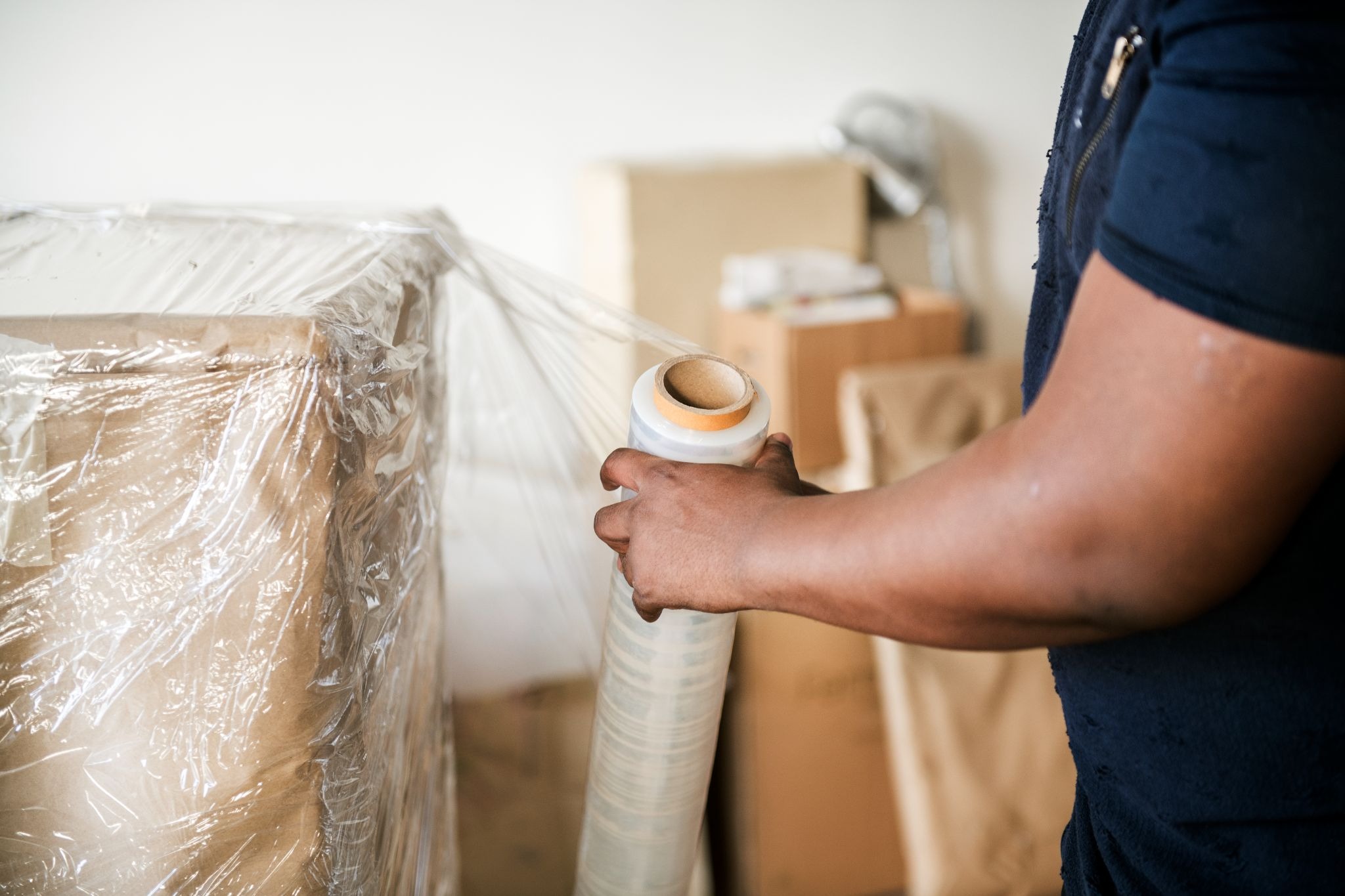 Worker wrapping a boxed item in clear stretch film.