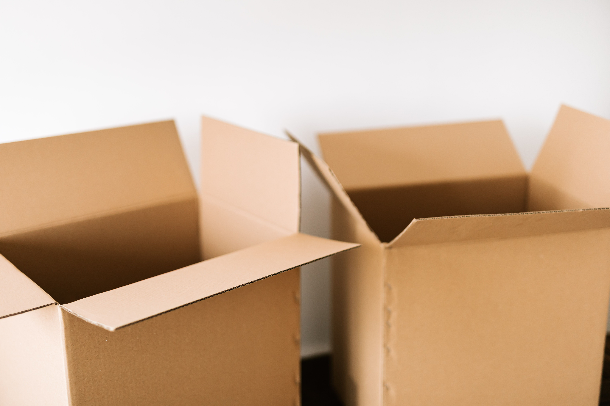 Close-up of open empty cardboard boxes arranged against a plain white wall.