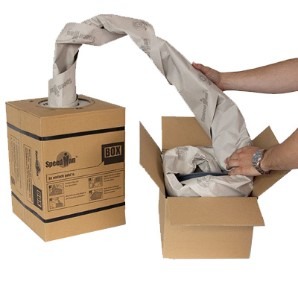 Hands pulling kraft paper from a dispenser box and packing it into a cardboard box as void fill.