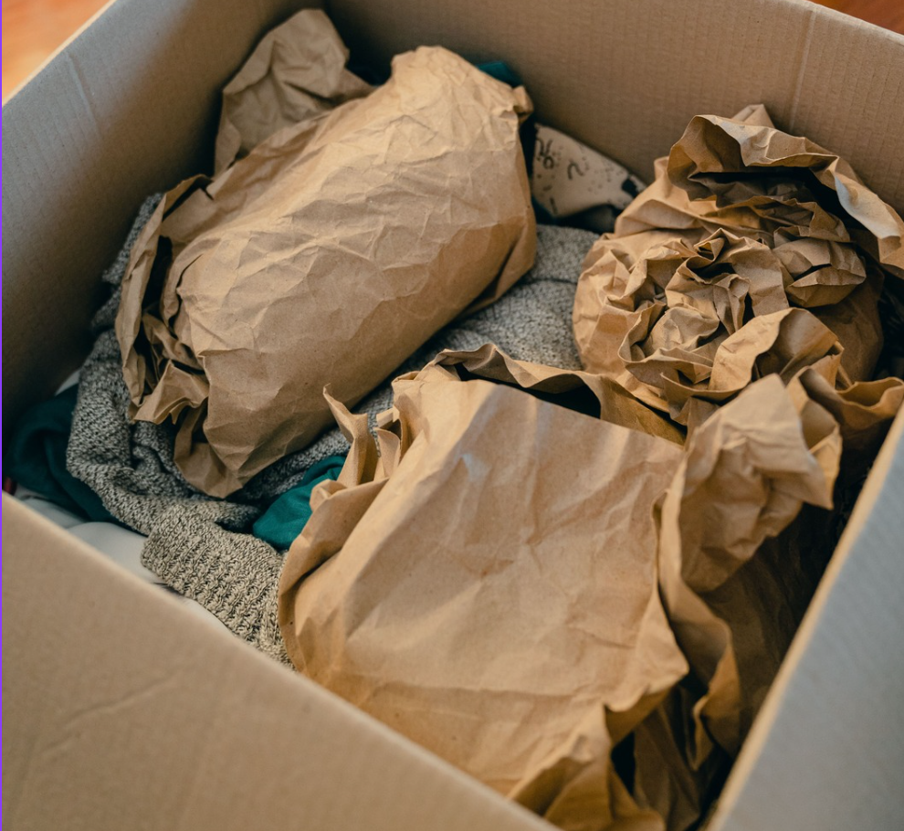 Crumpled kraft void fill packed around folded clothing inside a cardboard carton to stop movement in transit